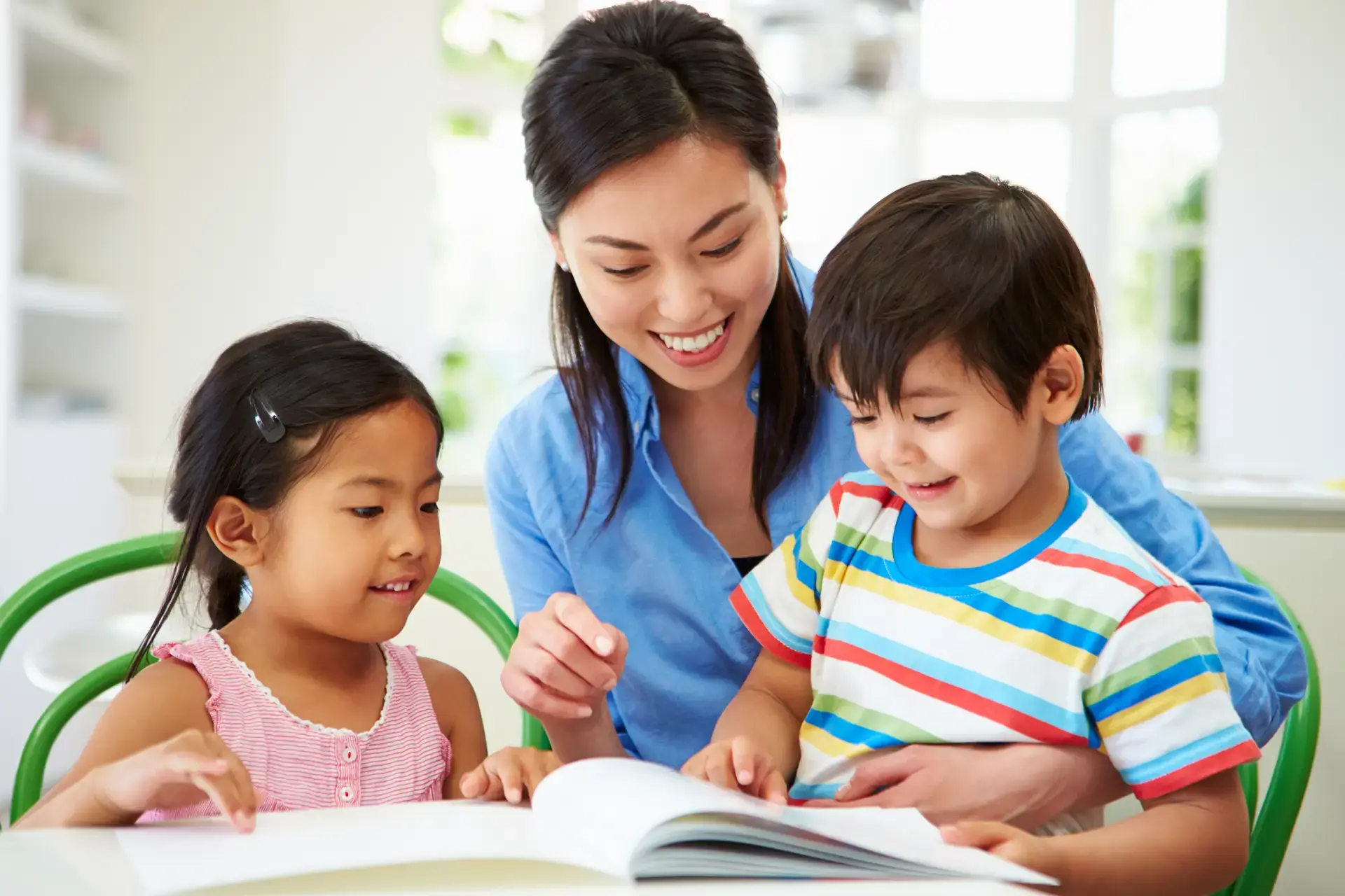 Asyanong batang babae at lalaki na nagbabasa ng libro kasama ang kanilang nanay.